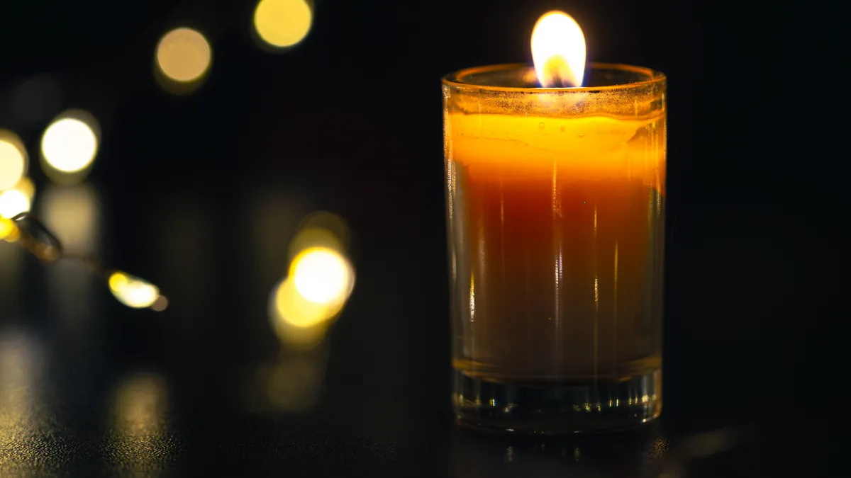 A single candle burning in a glass beside soft golden lights